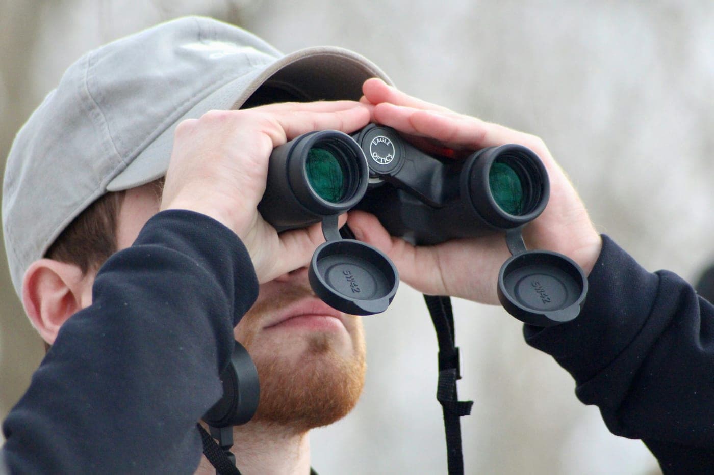A man in a gray cap looking through binoculars outdoors