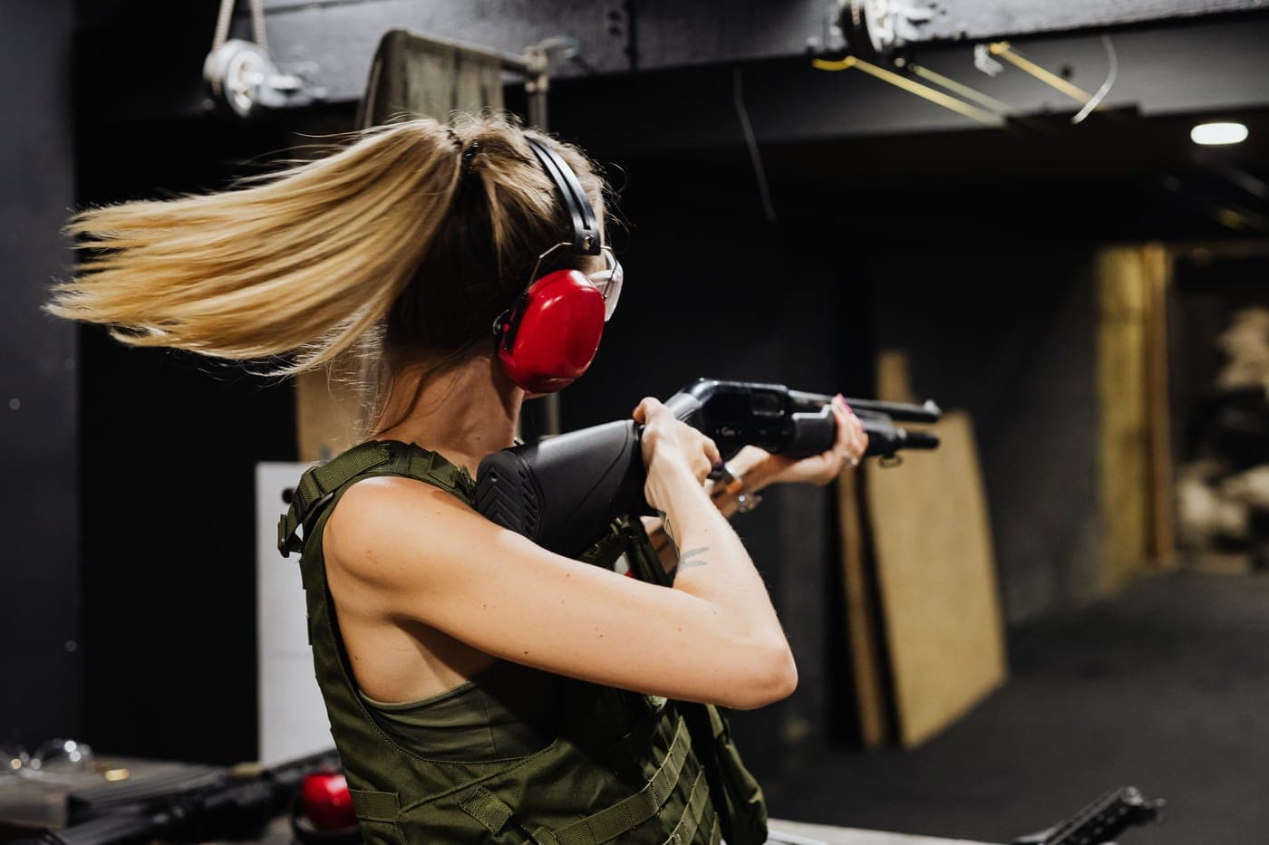 A shooter wearing ear protection holding a shotgun at an indoor range