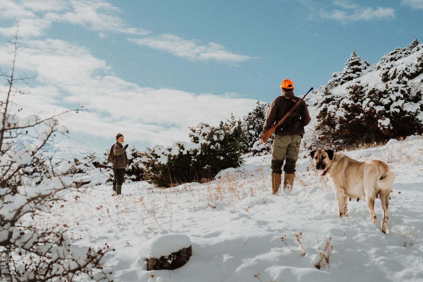 Two hunters and a dog crossing a snow-covered landscape