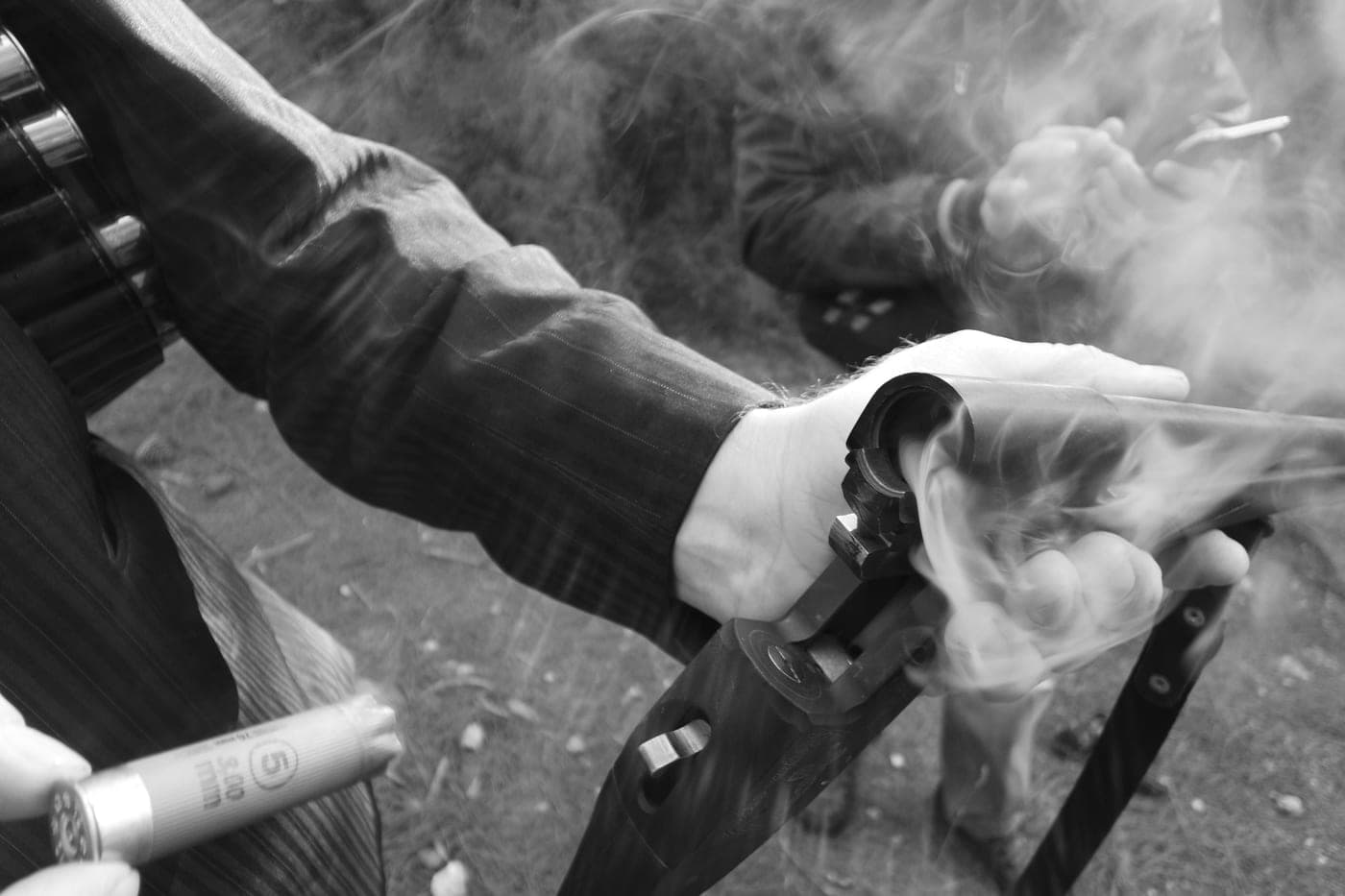 A hand holding a shotgun with smoke drifting from the action