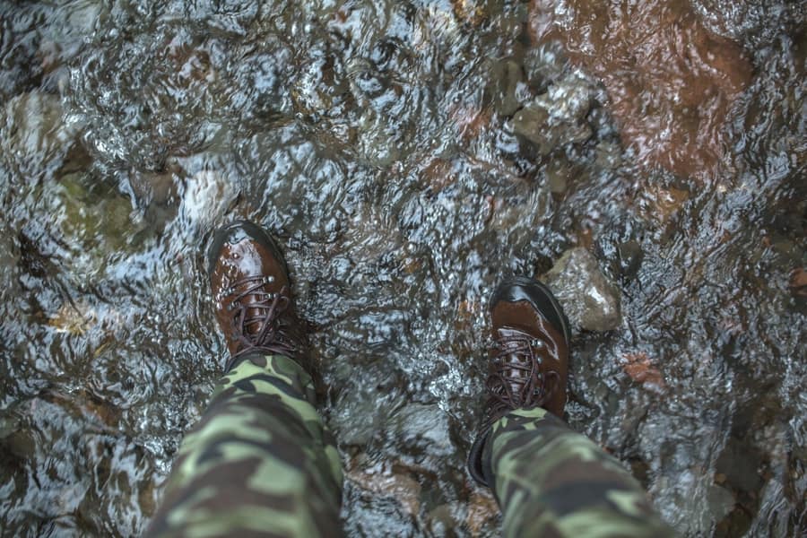 Illustrative stock photo: a person standing in a stream in camouflage pants and brown boots