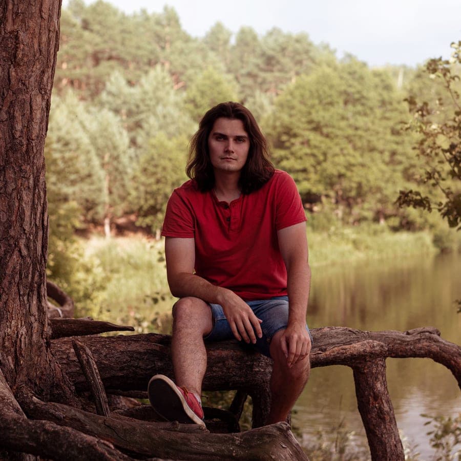 Illustrative stock photo: a man sitting on tree roots near a lake in the forest
