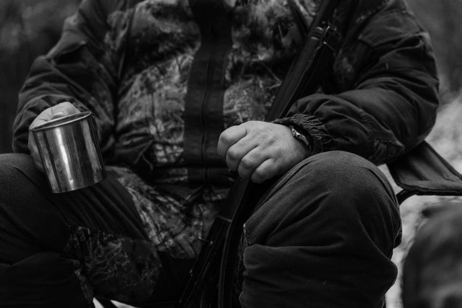 Illustrative stock photo: a hunter in camouflage sitting in the forest with a mug